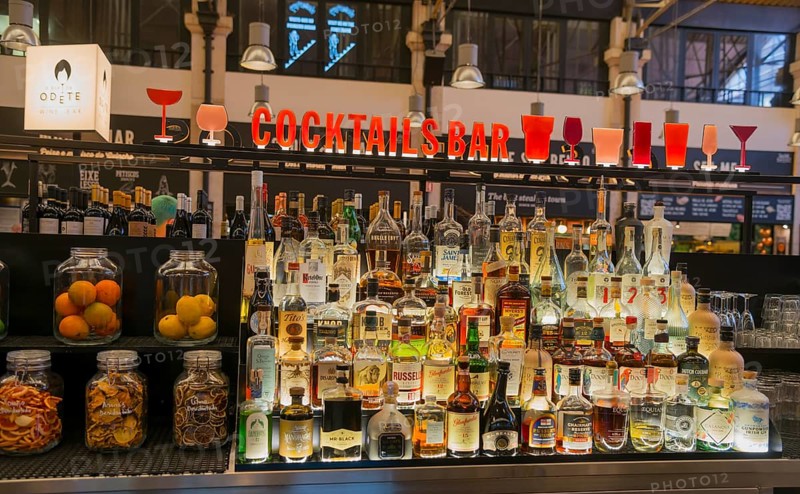 Eine gut bestückte Cocktailbar mit Flaschen verschiedener Spirituosen und bunter Beleuchtung in einer geschäftigen Umgebung, Mercado da Ribeira, Lissabon, Lisboa, Portugal, Europe