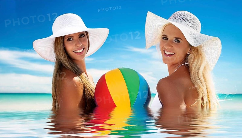 Two young woman in sun hats playing with a beach ball on the beach in the Caribbean