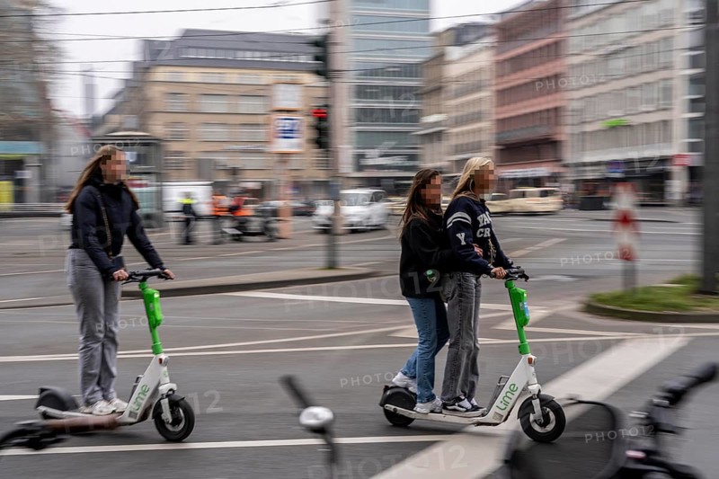 Young woman, two of them on an e-scooter, in the city centre, here at Neumarkt in Cologne, parked bikes and e-scooters at the roadside, bicycle lane, Cologne, North Rhine-Westphalia, Germany, Europe