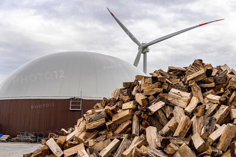 Biogas plant produces gas from various biomass, here the wood storage, the electricity is produced in combined heat and power plants with the biogas produced and sold to companies in the neighbouring industrial estate, the heat generated is fed into a local heating network, gas storage and wind power plant, Ense, North Rhine-Westphalia, Germany, Europe