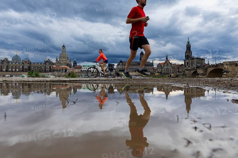 The silhouette of Dresden with a cyclist and a jogger and dark clouds behind the Church of Our Lady, reflected in a puddle on the Elbe cycle path, Elbe cycle path, Dresden, Saxony, Germany, Europe