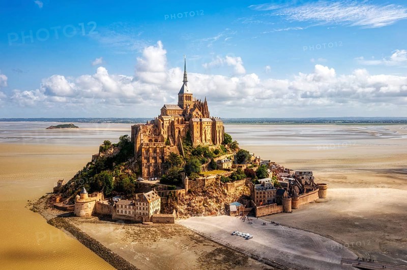 High-lying abbey on a rocky island, surrounded by sand and blue sky, Le Mont-Saint-Michel
