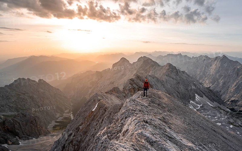 Mountaineer with helmet on a narrow rocky ridge at sunrise, crossing the Jubiläumsgrat, view of Höllental and Alpspitze, Wetterstein range, Bavaria, Germany, Europe
