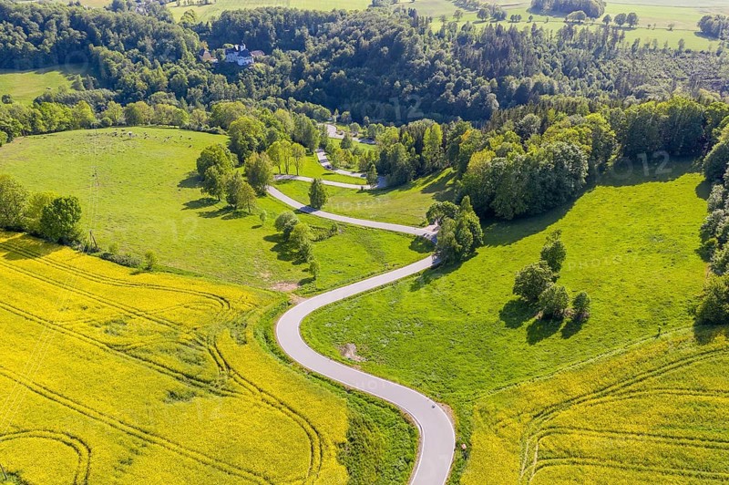Aerial view of the winding serpentine road between blossoming rapeseed fields from Reifland to Rauenstein, Rauenstein Castle in the background, Pockau-Lengefeld, Erzgebirge, Saxony, Germany, Europe
