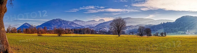 Wide green meadow in front of a mountain backdrop under a blue sky with light clouds, Bad Feilnbach