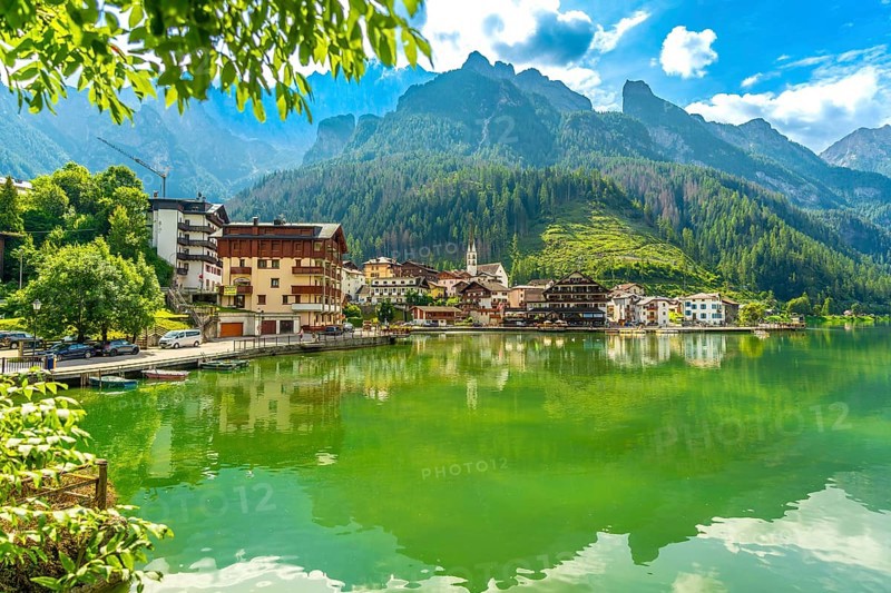 Tranquil summer scene of alleghe village reflecting on the emerald waters of lake alleghe, nestled amidst the stunning dolomites mountains in italy