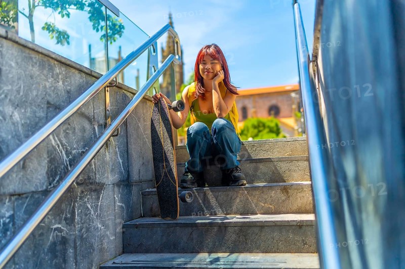 Low angle view portrait of a casual chinese girl sitting on urban stairs with her skateboard