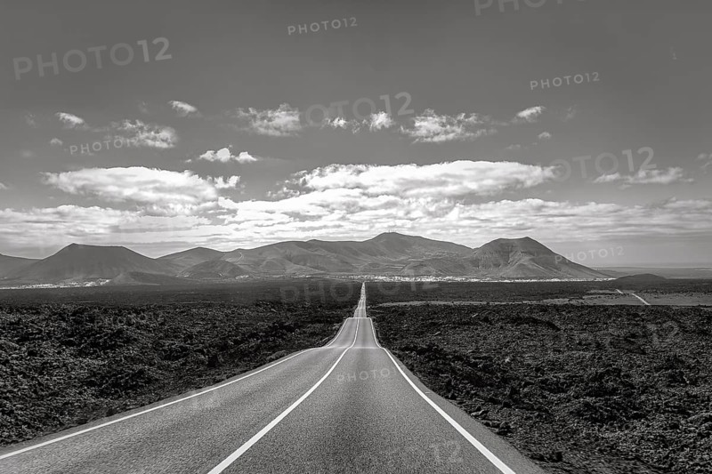 Empty endless country road through volcanic landscape, typical lava fields, Timanfaya National Park, fire mountains on the horizon, monochrome, Lanzarote, Canary Islands, Spain, Europe