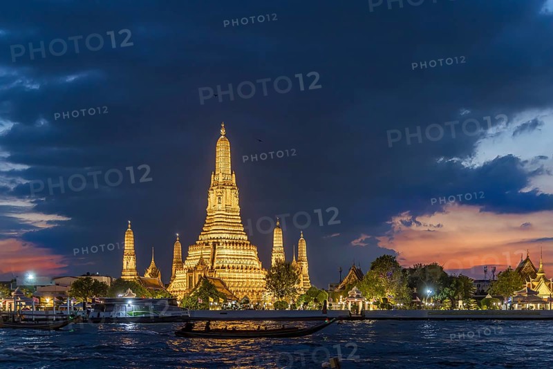 Wat Arun, Temple of Dawn at sunset with dark clouds. Boats on the Chao Phraya river. Tourist attraction in Bangkok, Thailand, Asia