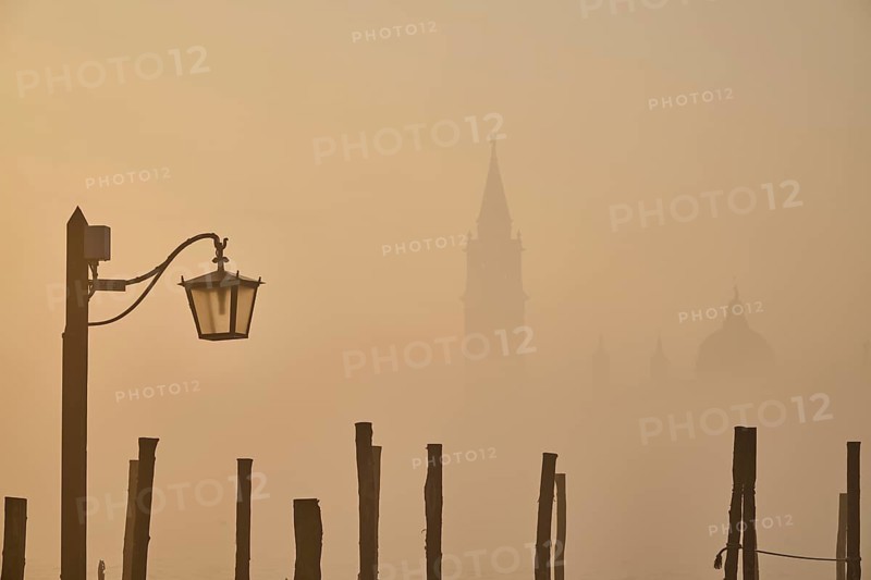 View from 'Colonna di San Marco e San Teodoro' on church 'Giorgio Maggiore' on a foggy morning at sunrise with a latern in front in Venice in winter, Italy, Europe
