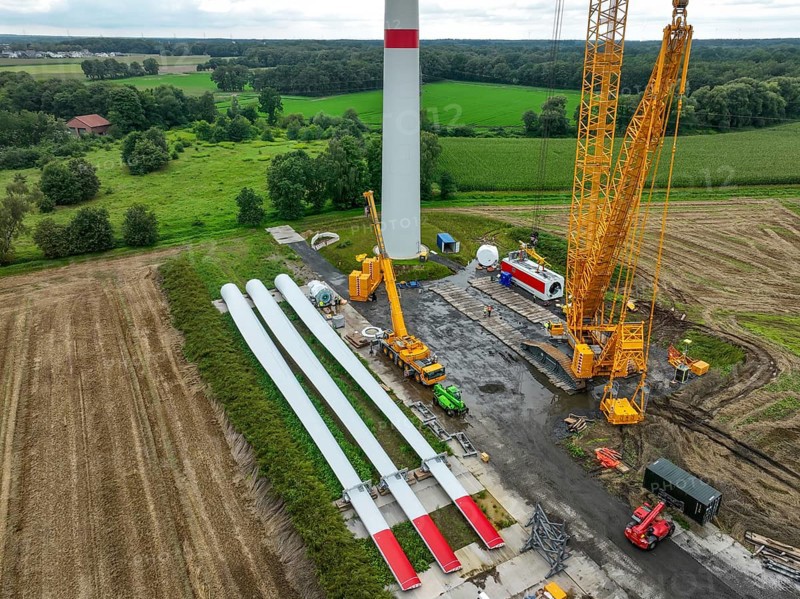 Dorsten, North Rhine-Westphalia, Germany, construction of a wind turbine, the first wind turbine of the Große Heide wind farm. A large mobile crane places the nacelle, the nacelle on the tower. The rotor blades, vanes and rotor hub are ready for assembly, Europe
