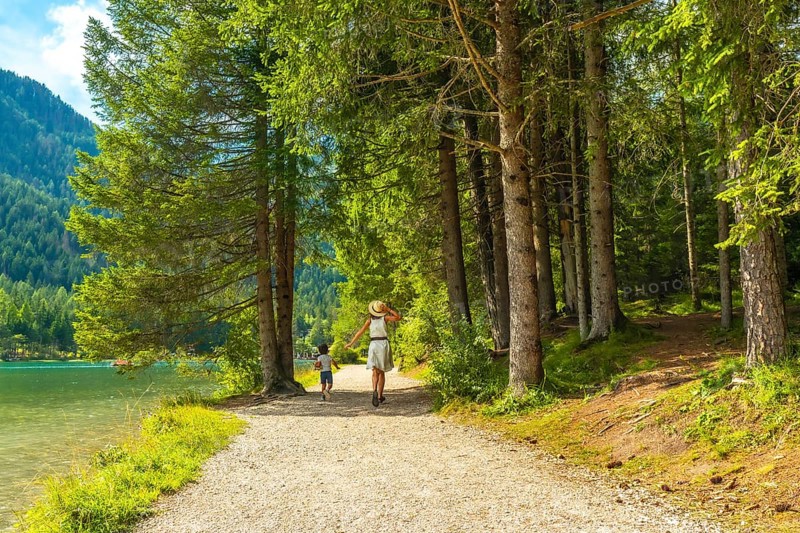 Tourists enjoying the stunning landscape of the dolomites while walking on a gravel path by the lake in the woods