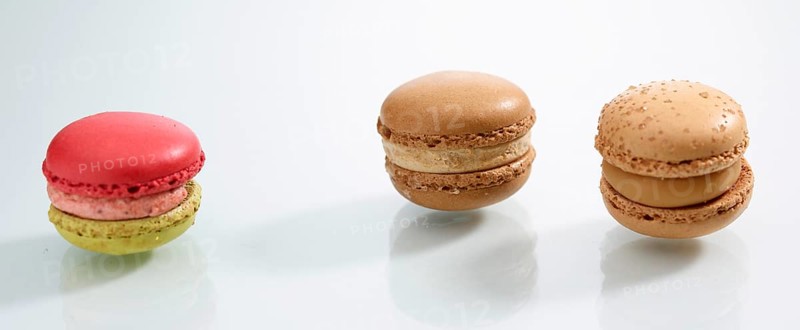 Three differently coloured macarons in front of a white background, studio shot