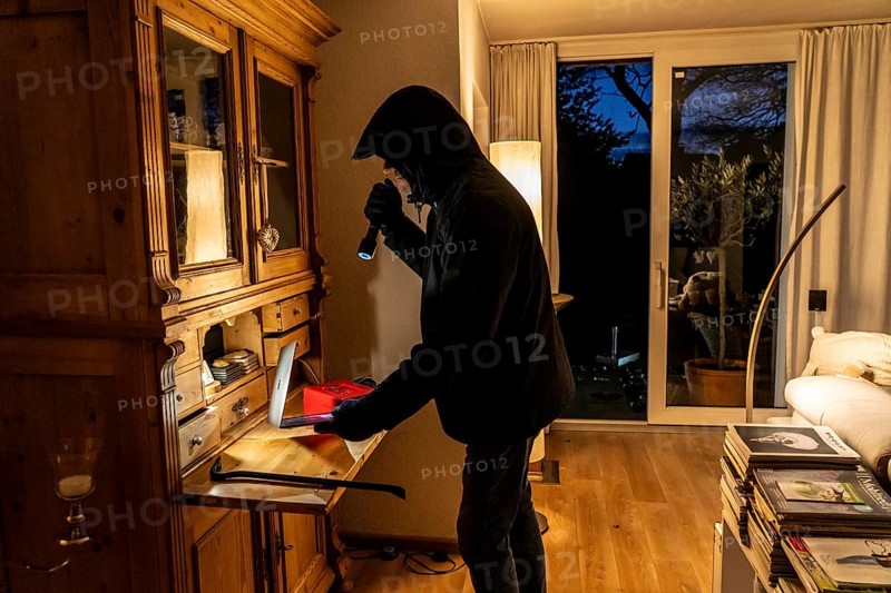 Symbolic image of a burglary, perpetrator has broken into a flat from the garden side and is looking for loot, computer, laptop, valuables, money, technology