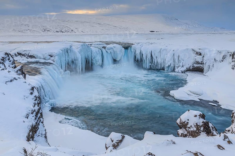 Icy waterfall and rapids in front of a mountain landscape, cloudy mood, snow, Godafoss, Iceland, Europe
