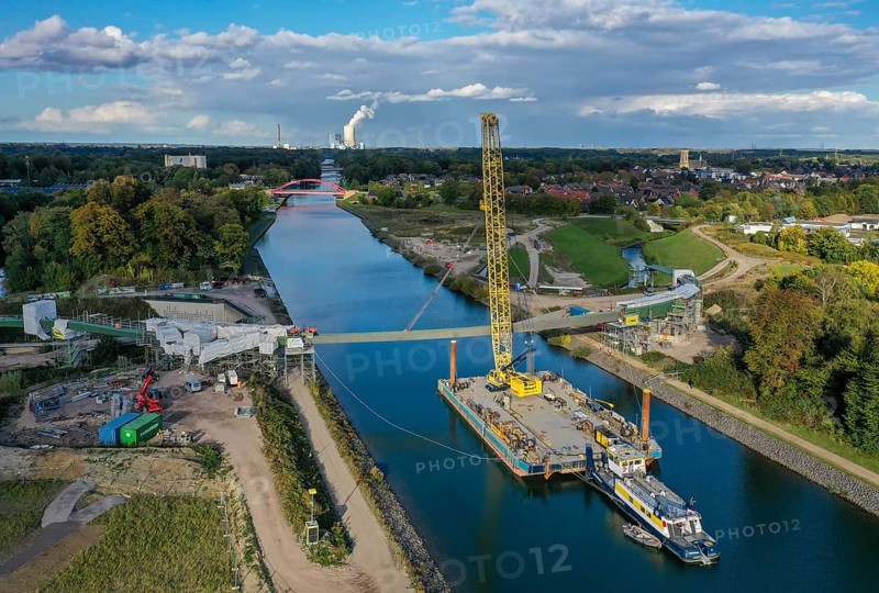 Castrop-Rauxel, North Rhine-Westphalia, Germany, new construction of a bridge -jump over the Emscher-, a floating crane on the Rhine-Herne Canal floating in the centre section of a foot and cycle bridge over the Emscher and the Rhine-Herne Canal. EMSCHERLAND construction project, a 37-hectare water and nature adventure park at the water crossroads of the Rhine-Herne Canal (right) and the renaturalised Emscher (from right to left) on the city boundary between Recklinghausen and Castrop-Rauxel. EMSCHERLAND will also be a garden of the future for the International Garden Exhibition 2027. Before the renaturalisation, the Emscher river system was an open, above-ground wastewater canal, mixed water canal with surface water and wastewater. The Uniper power plant Datteln 4 in the background, Europe