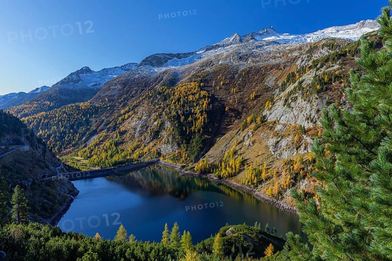 The Galgenbichl reservoir with a mountain forest in fall foliage on a bright sunny morning. Seen from the Malta Hochalm road. Carithia, Austria, Europe