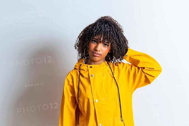 Studio portrait of a young woman wearing a yellow raincoat and scratching her head against a white background