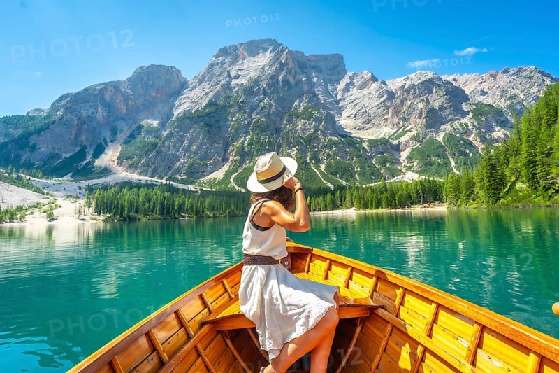 Young woman wearing a straw hat enjoying a boat trip on the turquoise waters of lake braies with the dolomites in the background during a summer day