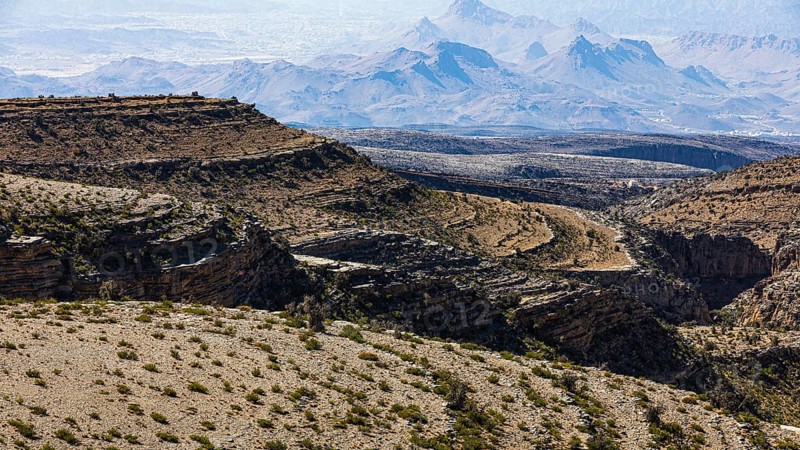 Slopes with barren vegetation and gorges, the mountains of the Hajar Mountains in the background, Arabian Peninsula, Sultanate of Oman