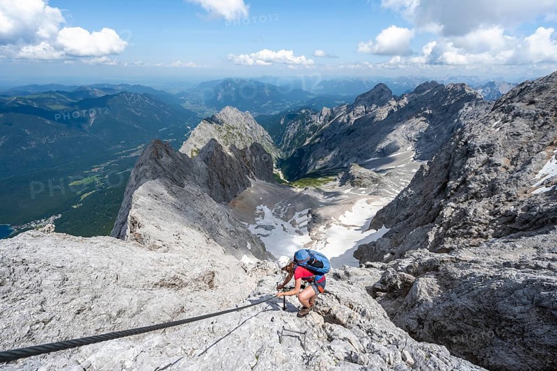Mountaineer with helmet in a secured via ferrata, Zugspitze via ferrata, ascent to the Zugspitze, view of mountain basin with snow field of the Höllentalferner and Höllental, Wetterstein range, Wetterstein range, Bavaria, Germany, Europe