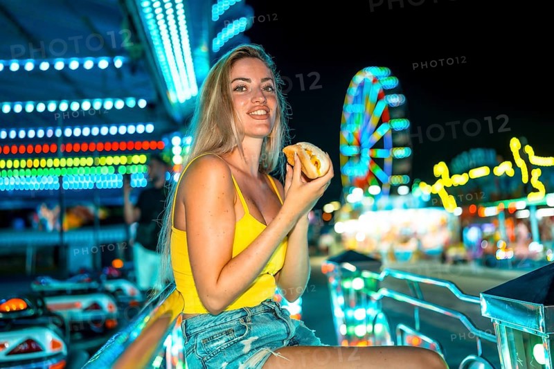 Blonde woman sitting eating a traditional hot dog at night fair