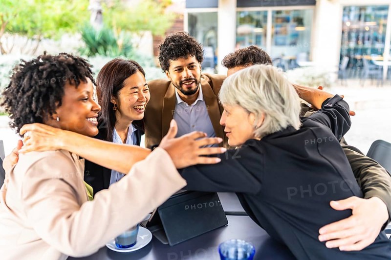 Business team of multi-ethnic people embracing together in circle standing in a cafeteria
