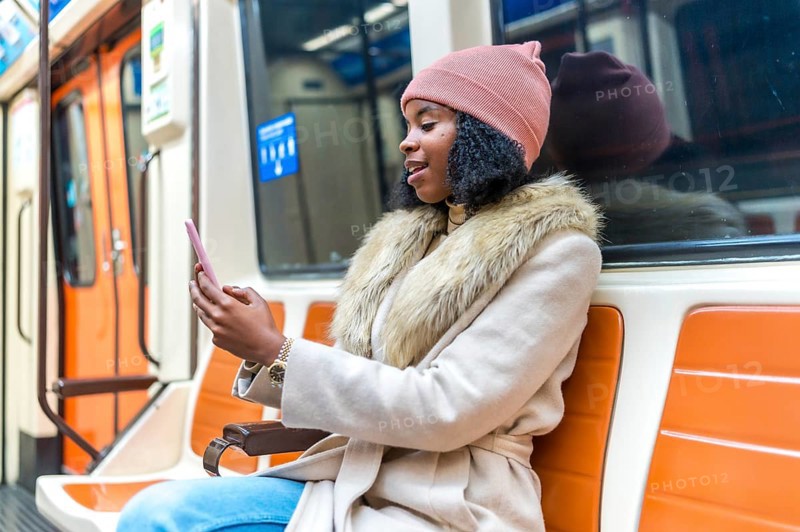 Stylish young woman commuting on a subway train, using her smartphone to browse social media and stay connected during her journey