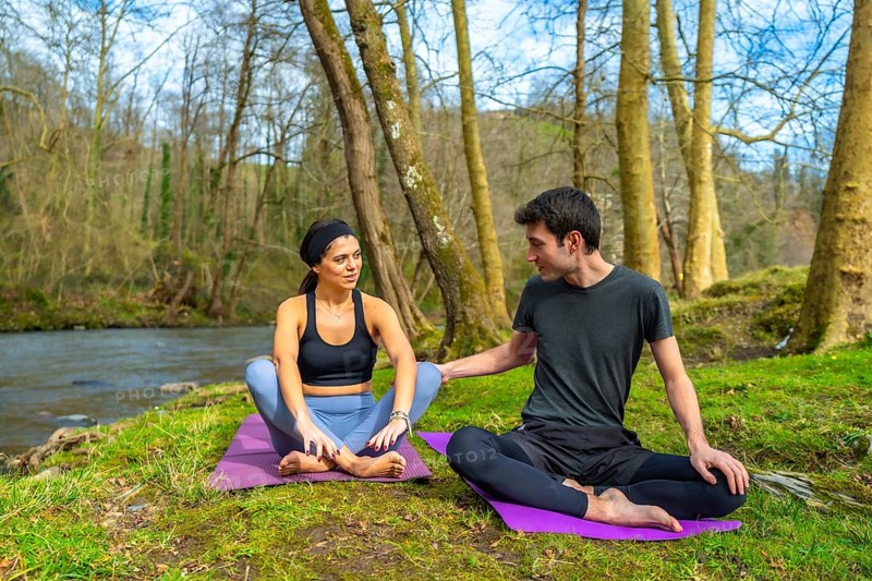 Yoga instructors performing meditation exercises by a river in a forest, enjoying the peace and quiet of nature