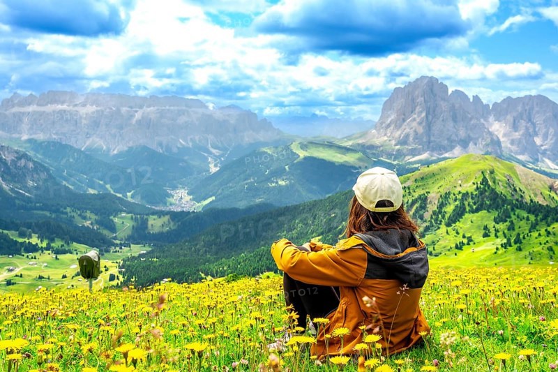 Hiker enjoying the stunning view of the seceda mountains in the dolomites during summer, surrounded by colorful wildflowers