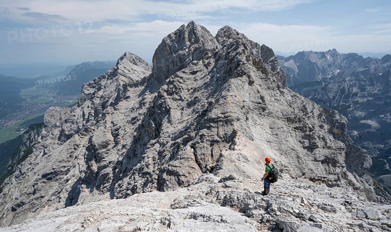 Mountaineer with helmet on a narrow rocky ridge, crossing the Jubiläumsgrat, view of rocky mountain peaks and Alpspitze, Wetterstein range, Bavaria, Germany, Europe