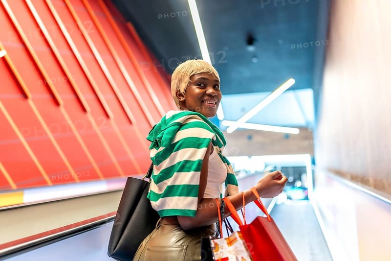 African woman using mechanical escalator in a shopping mall and turning to smile at camera