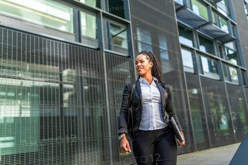 Portrait with low angle view and copy space of a casual latin businesswoman outside financial building holding laptop