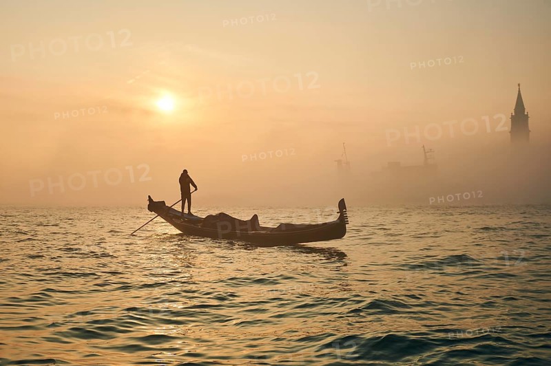View from 'Colonna di San Marco e San Teodoro' on gondolier in front of church 'Giorgio Maggiore' on a foggy morning at sunrise in Venice in winter, Italy, Europe