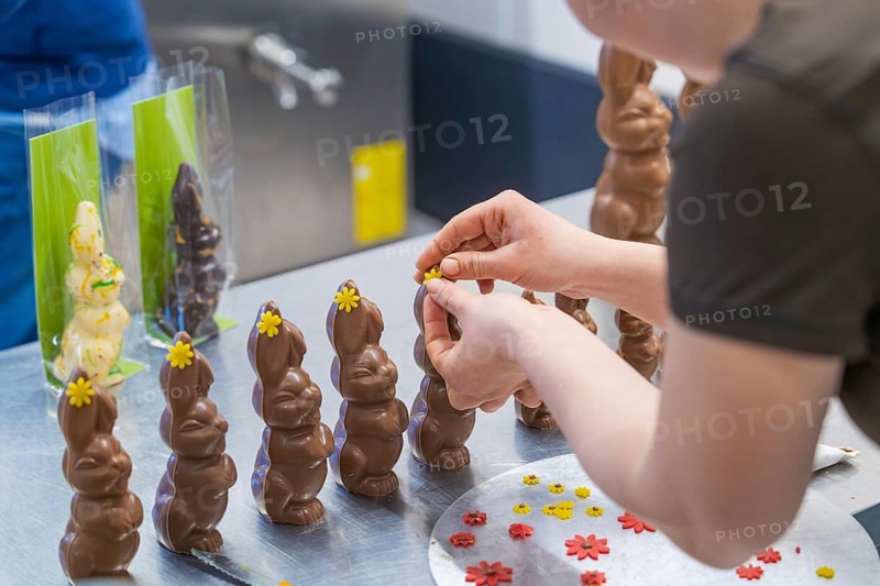 Person decorating several chocolate bunnies with flowers on a work table, Easter baking and chocolate moulding at Haselstaller Hof, Gechingen, Black Forest, Germany, Europe