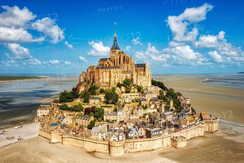 Impressive building complex on an island in a vast sandy landscape under a blue sky, Le Mont-Saint-Michel