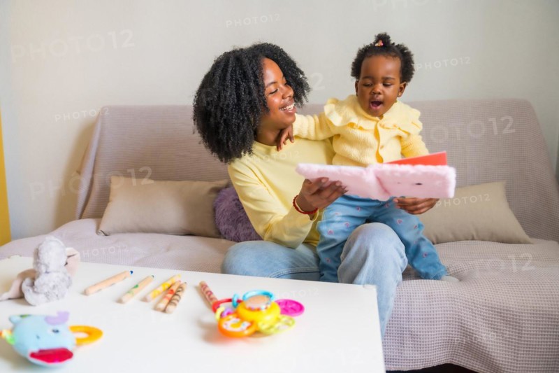 African mother and child smiling and reading a children's book sitting on the sofa