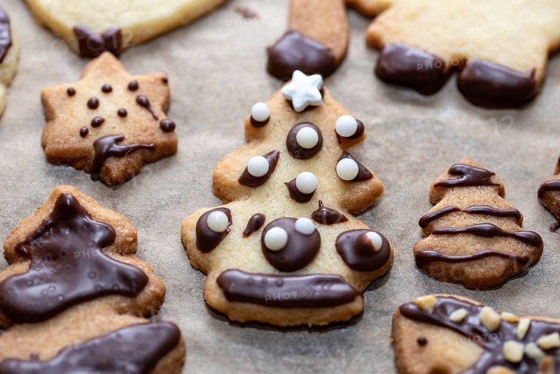Christmas biscuits with chocolate decoration in the shape of stars and fir trees on baking paper, Germany, Europe