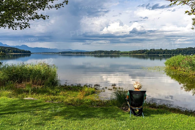 A woman sits on the shore of Lake Simssee near Bad Endorf, Bavaria, Germany, Europe