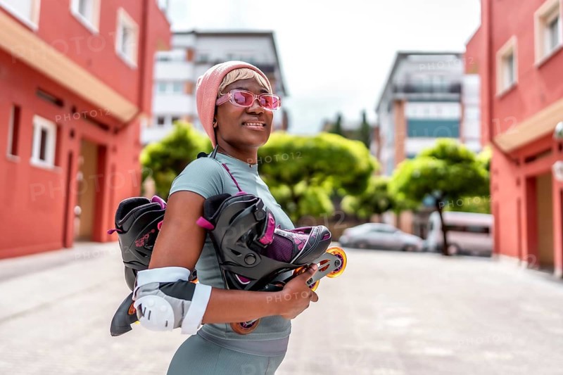 Side view of a modern african girl holding inline skates in the city