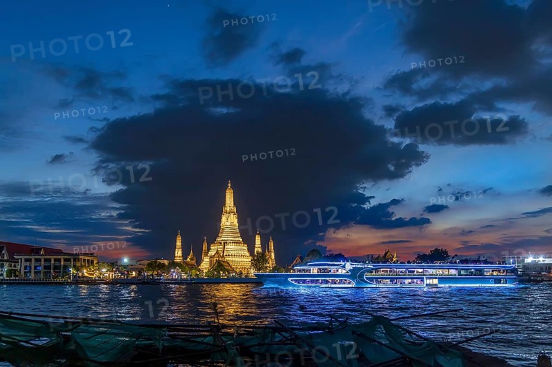 Wat Arun, Temple of Dawn at sunset with dark clouds. Boats on the Chao Phraya river. Tourist attraction in Bangkok, Thailand, Asia