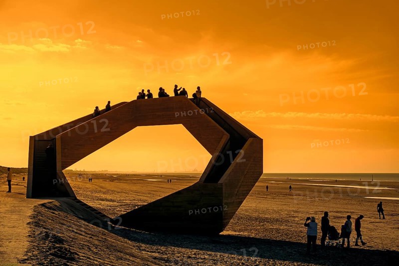 Westerpunt silhouetted against orange sunset sky, concrete sculpture on beach along North Sea coast at seaside resort De Panne, West-Flanders, Belgium, Europe
