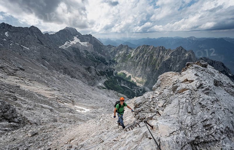Mountaineer with helmet climbing on rock, on a narrow rocky ridge, view of Zugspitze and Höllental in steep rocky mountain landscape, crossing the Jubiläumsgrat, Wetterstein range, Bavaria, Germany, Europe