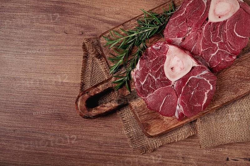 Knuckle on the bone, raw meat for ossobuco, on a wooden chopping board, with a sprig of rosemary, and spices, top view, no people