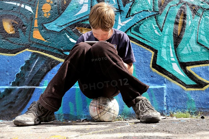 Ten-year-old boy playing with his Nintendo in front of a graffiti wall, football pitch, Germany, Europe