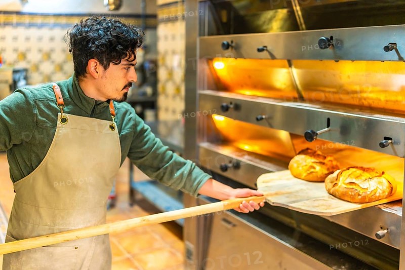 Latin young man baking bread in a traditional oven using a wooden peel