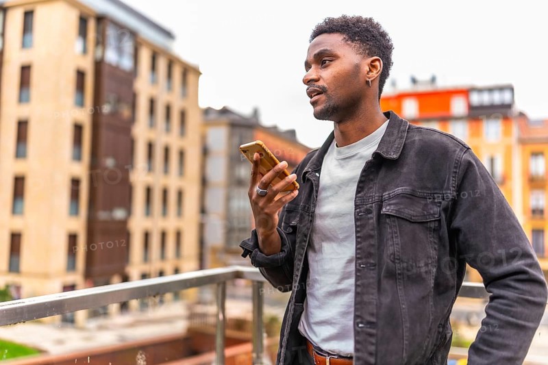 African man holding mobile sending a voice message with city views in the background