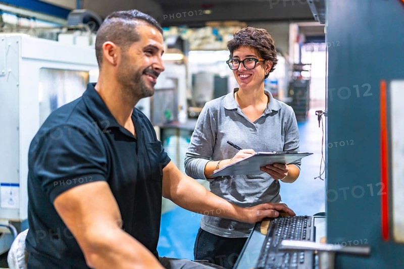 Manager and worker talking while working using computer in a cnc metal factory