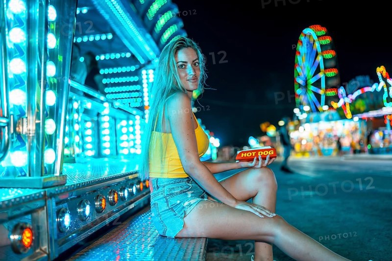 Side view photo of a woman in a night fair about to eat a hot dog
