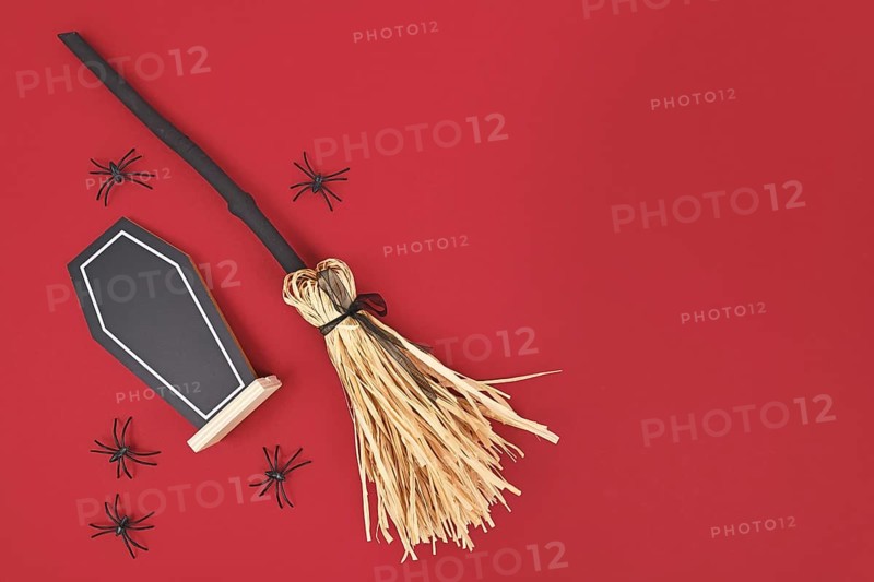 Halloween witch broom, coffin shaped chalkboard and spiders on dark red background with copy space